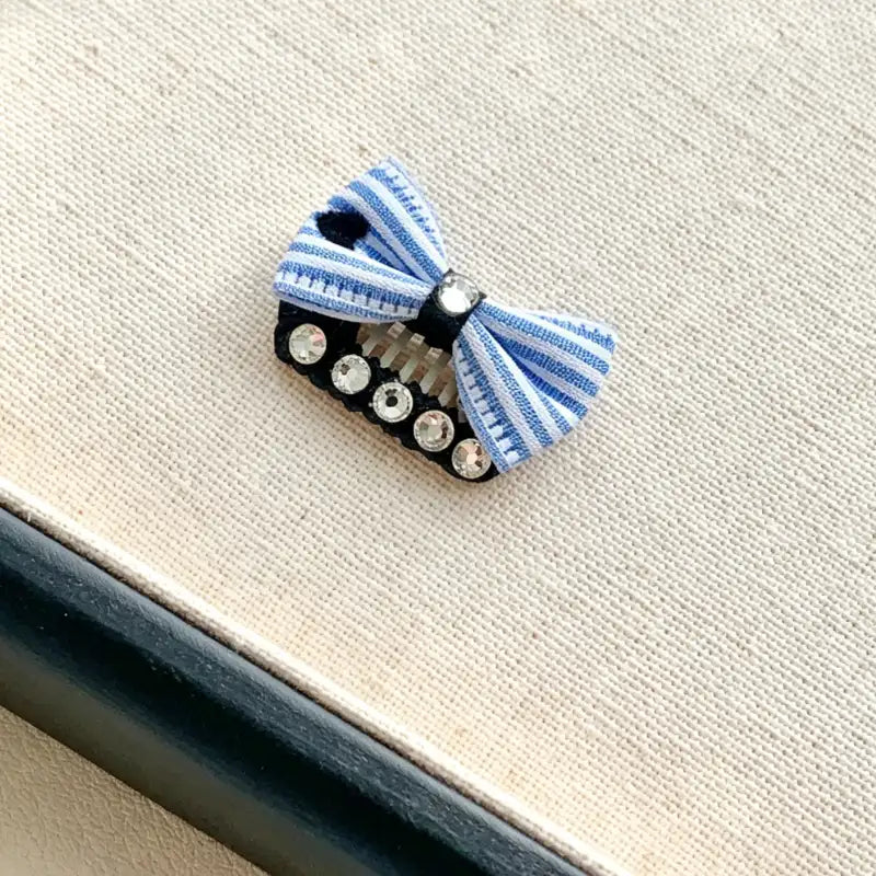 Blue and white striped bow hair clip with rhinestones on a textured beige background