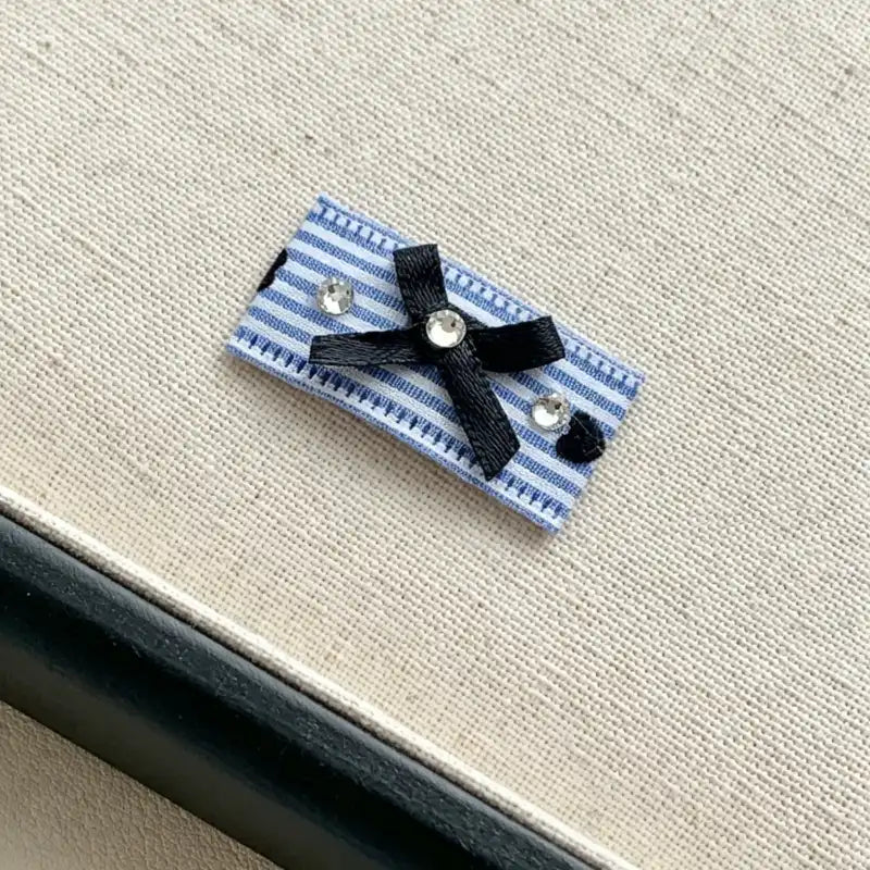 Blue and white striped fabric clip with a black bow and decorative elements on a textured surface.