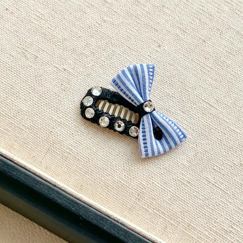 Hair clip with blue and white striped bow and decorative elements on a beige surface